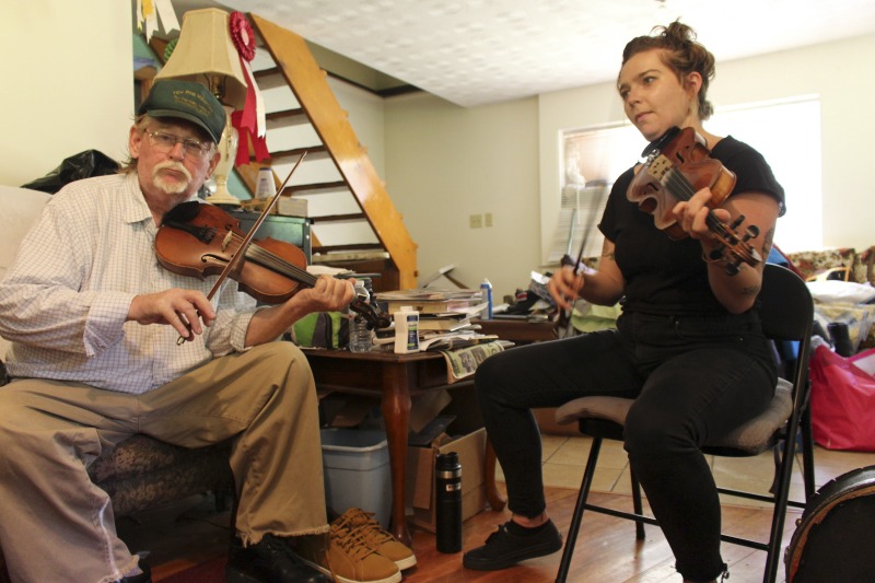 ["John D. Morris of Ivydale led an apprenticeship in old-time fiddle and stories of Clay County with Jen Iskow of Thomas as part of the 2018 West Virginia Folklife Apprenticeship Program, supported in part by the National Endowment for the Arts. John D. MorrisBorn in Ivydale, Clay County, into a family steeped in traditional music, David and John Morris learned from family and neighbors, including banjo player Jenes Cottrell and fiddler French Carpenter. After David returned from Vietnam in 1968, the brothers began organizing musical get-togethers and, in 1969, held the first Morris Family Old-Time Music Festival that same year. The festival became a major traditional music event in Clay County and filmmaker Bob Gates documented the 1972 festival in his film The Morris Family Old-Time Music Festival.Members of The Morris Brothers band included Pocahontas County old-time banjo player Dwight Diller and the late North Carolina harmonica player John Martin. Playing a mix of old-time, bluegrass, and country styles, including some of Davids original music, the group played together through the mid-70s, releasing an LP in the late 60s, Music As We Learned It, and two live shows on eight-track tapes. John, a traditional fiddler, and David, a singer, songwriter, and guitarist, were involved in union and environmental activities from the late 1960s through the 1970s. They were also instrumental in establishing the first Vandalia Gathering at the Cultural Center in 1977.The Morris Brothers music was featured in Barbara Kopples 1976 film Harlan County, USA. David, who passed away in 2016, contributed music to Kopples 2015 film about Vietnam vets, Shelter.John lives in Ivydale and plays fiddle at music events across West Virginia. He is a rich source of information about the history of old-time music in central West Virginia, and one of the few native fiddlers of his generation to continue the older style of playing.Morris was awarded the National Endowment for the Arts National Heritage Fellowship, the nations highest honor in the folk and traditional arts, in 2020.Jen IskowJen Iskow is an artist, designer, musician, and community organizer based in Thomas, West Virginia. Born and raised in Rockville, Maryland, Jen grew up learning to play blues and punk music. It wasnt until she moved to Morgantown in 2009 for college that she was introduced to old-time music at the weekly Brew Pub jam hosted by Stewed Mulligan. After graduating from West Virginia University, she finally settled in Elkins, West Virginia and accepted a position as the Marketing Coordinator for the Augusta Heritage Center. Suddenly being surrounded by so many talented traditional artists, Jen was immersed into the music and inspired to learn to play fiddle. After studying under talented fiddlers such as Scott Prouty, Erynn Marshall, Jesse Wells, Ben Townsend, John Harrod, and more, Jen met John Morris at his house in Ivydale, and the rest is historySee our feature on Morris apprenticeship with Iskow here: https://wvfolklife.org/2018/11/09/2018-master-artist-apprentice-feature-john-morris-jen-iskow-old-time-fiddling-and-stories-of-clay-county/"]%